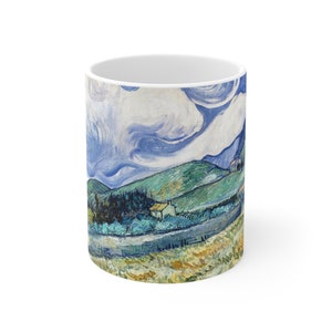 Può includere: Una tazza in ceramica bianca con un'immagine colorata di un dipinto di paesaggio. Il dipinto presenta colline ondulate, un cielo blu con nuvole bianche e un piccolo villaggio in lontananza. I colori sono vivaci e le pennellate sono visibili.