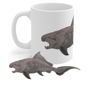 May include: White ceramic mug featuring a black and white illustration of a prehistoric fish with sharp teeth. The fish is depicted twice, once on the mug and once in a smaller size below the mug.