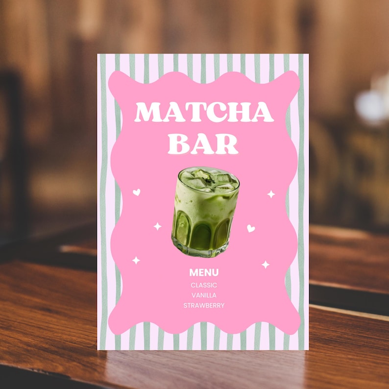 May include: A Matcha Bar menu sign with a pink background and green striped border. The sign features the words "Matcha Bar" in white, a photo of a matcha drink, and a list of flavors: Classic, Vanilla, and Strawberry.
