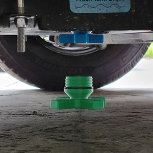 May include: A green plastic fresh water tank drain plug with a star-shaped handle. The plug is threaded and has a black O-ring. A blue sign above the tire reads "Fresh Tank Drain".