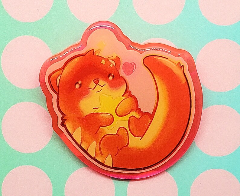 May include: A sticker featuring a cartoon otter in shades of orange and yellow, holding a star-shaped object. The otter is surrounded by a pink outline with a heart, set against a pink and blue polka dot background.