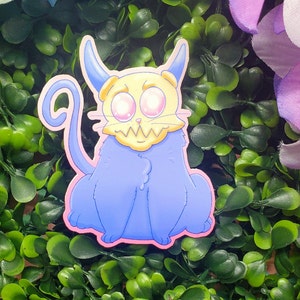 May include: A sticker featuring a cartoon cat-like creature with a light blue body, a yellow skull-like face, and pink eyes. The sticker has a pink border and is set against a backdrop of green foliage and purple flowers.