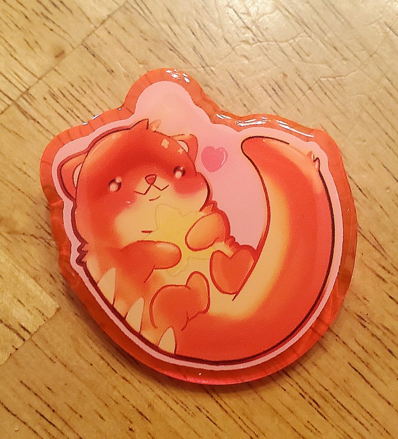 May include: A colorful, cartoon-style sticker featuring an otter holding a heart-shaped object. The otter is primarily orange with white accents, set against a pink background with a heart. The sticker has a glossy finish and a clear border.