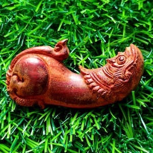 Può includere: Una statuetta in legno intagliata a mano di una creatura mitologica con una finitura rosso-marrone. La creatura ha una coda di pesce e una testa con una grande bocca aperta.