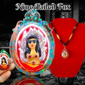 Può includere: Un ciondolo rosso e bianco a forma di volpe a nove code con un viso di donna e nove code. Il ciondolo è racchiuso in resina trasparente con glitter. Il ciondolo è su un cordino marrone.