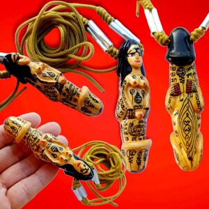 Könnte beinhalten: Drei Holzanhänger mit aufwendigen Schnitzereien und goldenen Akzenten. Jeder Anhänger zeigt ein anderes Design, darunter eine weibliche Figur, eine männliche Figur und eine stilisierte Figur. Die Anhänger sind an einer gelben Schnur befestigt.