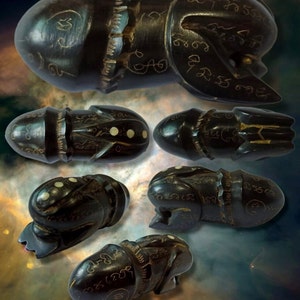 Può includere: Cinque amuleti in legno nero con intagli intricati e punti bianchi. Gli amuleti hanno la forma di un fallo e hanno diversi simboli e caratteri incisi.