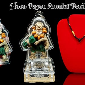 Puede incluir: Un colgante de plástico transparente con una pequeña figura verde y marrón en su interior. La figura lleva un paño verde y un collar de cuentas. El colgante está sobre un soporte de plástico transparente. El texto "Hoon Payon Amulet Pendant" está en la parte superior de la imagen.