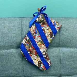 以下が含まれることがあります： 青と白のストライプ柄と犬の模様のクリスマスストッキング。ストッキングは金のベルと青いリボンで飾られています。