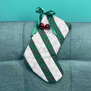 以下が含まれることがあります： 緑と赤のストライプと白い水玉模様の白いクリスマスストッキング。ストッキングは緑のサテンのリボンと赤いオーナメント2つで飾られています。