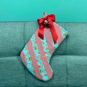 May include: A red and white striped Christmas stocking with a blue background and a reindeer pattern. The stocking has a red bow and a bell at the top.