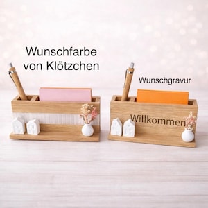 Könnte beinhalten: Zwei rechteckige Schreibtisch-Organizer aus Holz mit Stiftehaltern, Notizzettelhaltern, zwei kleinen weißen Hausfiguren und einer winzigen weißen Vase mit Trockenblumen. Der linke Organizer hat einen weißen Streifen, der rechte trägt den Text Willkommen.