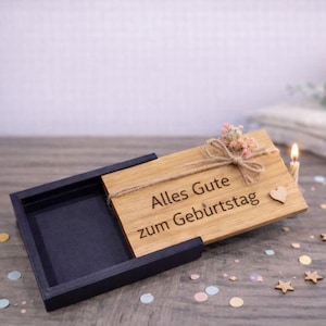 Könnte beinhalten: Eine rechteckige Holzschachtel mit Schiebedeckel, auf dem der Text Alles Gute zum Geburtstag eingraviert ist. Der Deckel ist mit einer kleinen Kordelschleife, getrockneten rosa Blumen und einem winzigen Holzherz verziert. Der Boden ist dunkelgrau.