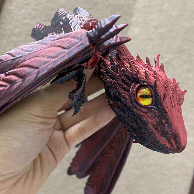 Puede incluir: Una peque&ntilde;a figura de drag&oacute;n rojo con detalles negros y ojos amarillos. El drag&oacute;n tiene alas y est&aacute; en posici&oacute;n de vuelo.
