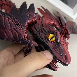Puede incluir: Primer plano de una figura de drag&oacute;n impresa en 3D de color rojo y negro con una superficie texturizada detallada y un ojo amarillo brillante.