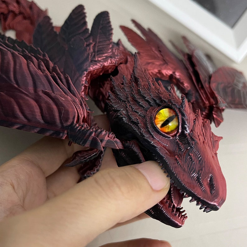 Puede incluir: Primer plano de una figura de drag&oacute;n impresa en 3D de color rojo y negro con una superficie texturizada detallada y un ojo amarillo brillante.