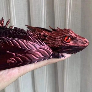 Puede incluir: Una figura de drag&oacute;n impresa en 3D con un acabado met&aacute;lico rojo. El drag&oacute;n tiene un cuerpo detallado y texturizado y un solo ojo rojo.