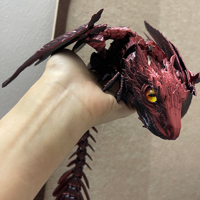 Puede incluir: Una figura de drag&oacute;n rojo impresa en 3D con ojos amarillos. El drag&oacute;n est&aacute; en posici&oacute;n con las alas extendidas y la cola enroscada. La figura est&aacute; hecha de un pl&aacute;stico texturizado y detallado.
