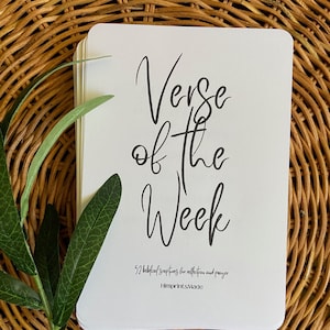 Puede incluir: Una pila de tarjetas blancas con el texto "Verse of the Week" escrito en cursiva negra. Las tarjetas están sobre una superficie de mimbre tejido. El texto en la parte inferior de las tarjetas dice "52 escrituras bíblicas para la reflexión y la oración" e "ImprintsMade".