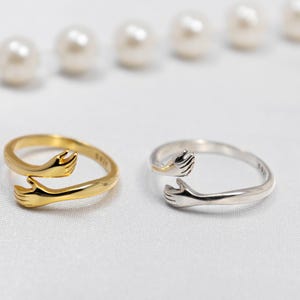 May include: Two silver rings with a design of two hands reaching out to each other. One ring is gold and the other is silver.