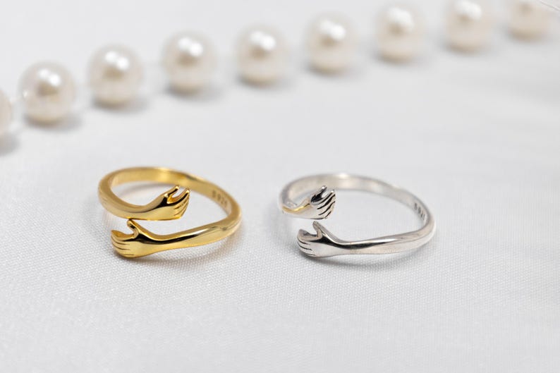 May include: Two silver rings with a design of two hands reaching out to each other. One ring is gold and the other is silver.