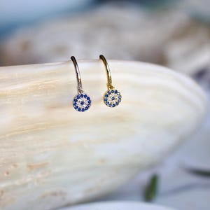 May include: A pair of hoop earrings with a circular charm featuring a blue and white design. One earring is gold-toned, the other is silver-toned. The earrings are displayed on a white surface.