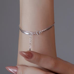 May include: A silver chain bracelet with a delicate chain and a small charm hanging from it.