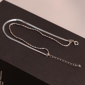 May include: A silver chain bracelet with a delicate, thin chain and a thicker, flat chain. The bracelet has a lobster clasp and an extension chain.