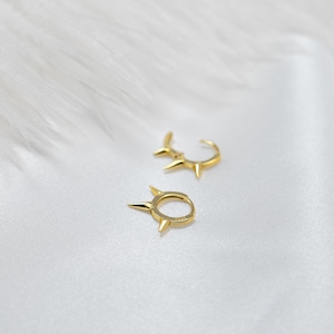 May include: Two gold hoop earrings with a pointed design. The earrings are on a white background.
