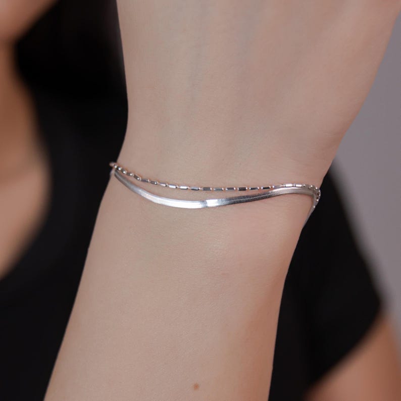 May include: A silver chain bracelet with two different styles of chain. The bracelet is layered with a thin, delicate chain and a thicker, more substantial chain.
