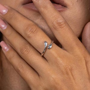 May include: A silver ring with two hands clasped together, the ring is worn on a person's finger.