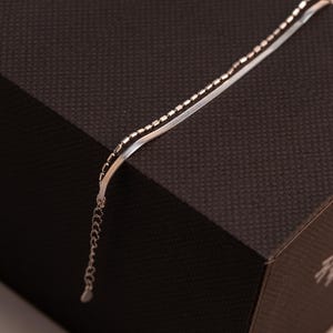 May include: A silver chain necklace with two different styles of chain. The chain is on a brown textured surface.