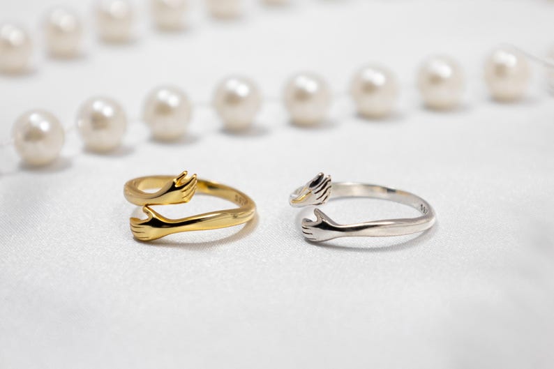 May include: Two adjustable rings with a design of two hands embracing each other. One ring is gold and the other is silver.