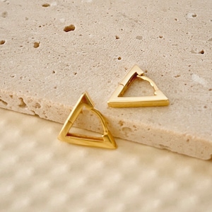 May include: A pair of gold triangle hoop earrings. The earrings are simple and elegant, and would make a great addition to any jewelry collection.