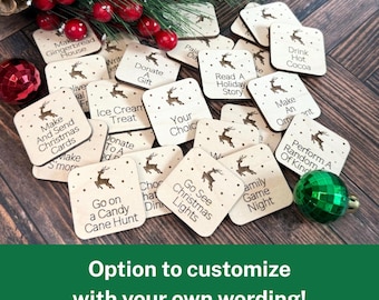 May include: Wooden Christmas activity tiles with various festive prompts like "Go See Christmas Lights" and "Make Gingerbread House." Each tile features a reindeer design. A green ornament and pine needles are also visible.