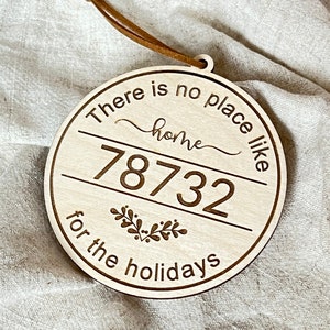 May include: Round wooden ornament with a leather strap. The ornament has the text "There is no place like home for the holidays" and the number "78732". The text and numbers are in a dark brown color.