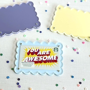May include: Three decorative frames in purple, yellow, and light blue, each with a scalloped edge. The light blue frame holds a Starbucks gift card with the words "YOU ARE AWESOME" in red and yellow. Colorful confetti is scattered around.