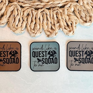 May include: Three square coasters with rounded corners, each featuring the text "sounds like a QUEST to SQUAD me" in black. The coasters are in shades of brown, blue-green, and gray, with a dragon graphic.