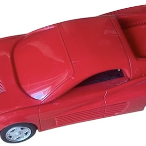 Può includere: Un'auto giocattolo rossa con il logo Ferrari. L'auto ha un design elegante con ruote argentate e un cavo nero attaccato sul retro. L'auto è lunga circa 30 cm.