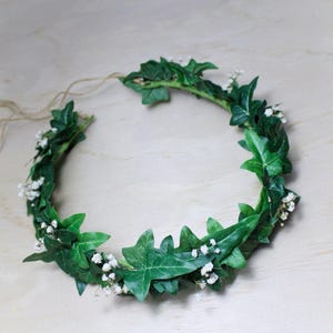 May include: A green leaf crown with white flowers woven into the leaves. The crown is made of natural materials and is perfect for a wedding or other special occasion.