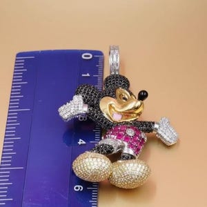 Puede incluir: Un colgante con un dise&ntilde;o estilizado de Mickey Mouse. El colgante tiene una cara dorada, un cuerpo negro y detalles en rojo y blanco. El colgante mide aproximadamente 5 cm de altura.