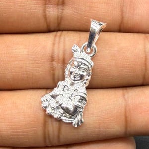 May include: A polished silver-toned metal pendant featuring a detailed relief sculpture of a figure with a crown and traditional attire, designed with a small integrated loop at the top for attachment to a necklace chain or cord.