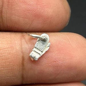 Può includere: Un piccolo ciondolo color argento a forma di sandalo. Il ciondolo ha un anello nella parte superiore per il fissaggio a un braccialetto o una collana. Il sandalo ha delle trame dettagliate.