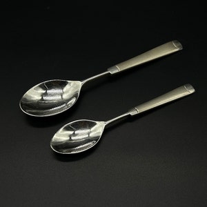 May include: Two silver spoons with polished, reflective surfaces. The spoons have simple, rounded handles.
