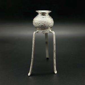 May include: A silver decorative stand with a round top and three legs. The stand is decorated with floral patterns.