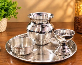 May include: A polished silver-toned metal set consisting of a round tray, a small bowl, a wide-mouthed pot with a rounded body, and a pedestal-based cup. Each piece features a smooth, reflective surface with subtle horizontal grooved detailing.