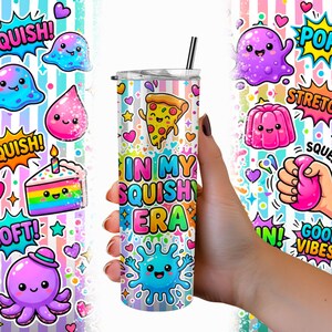 May include: A cylindrical tumbler with a metal straw featuring a colorful pattern of cartoon characters, pizza, cake, and hearts against a pastel striped background. The text "IN MY SQUISHY ERA" is printed in the center in bright, multi-colored letters.