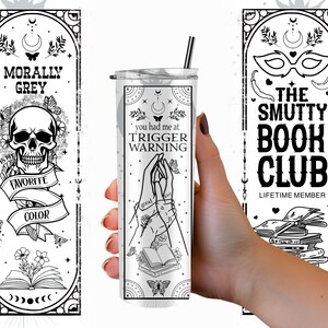May include: A black and white tumbler with the text "you had me at trigger warning" and a graphic of two hands holding a book. The tumbler is surrounded by a black and white border with stars and butterflies.