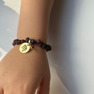 May include: A brown and amber beaded bracelet with a gold charm featuring the astrological symbol for Virgo.