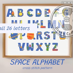 May include: Cross-stitch pattern of the alphabet with a space theme. Each letter is designed with planets, rockets, and stars in blue, orange, and green. The framed artwork includes the text "all 26 letters" and "SPACE ALPHABET cross stitch pattern."